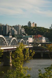 Bridge over river by buildings in city against sky