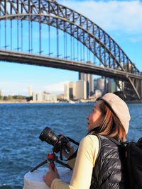 Man photographing bridge over river in city against sky