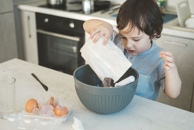 The little boy pours the prepared cake mix into the bowl with the rest of the ingredients.