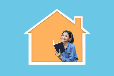 Portrait of a smiling young woman standing against blue wall