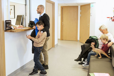 Father and son at reception counter while family waiting on bench at orthopedic clinic