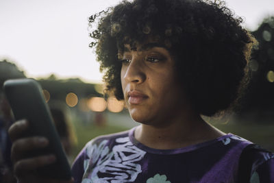 Transgender woman with curly hair using smart phone during sunset