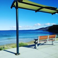 Empty bench at shore against blue sky