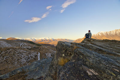 Rear view of man standing on rock against sky