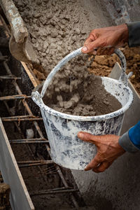 Close-up of hand filling bucket with concrete at construction site
