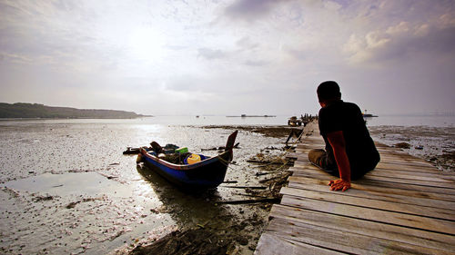 Rear view of men on boat at beach against sky