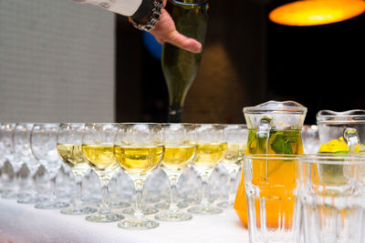 Glasses are filled with alcoholic beverages, the waiter's hand pours white wine from a bottle