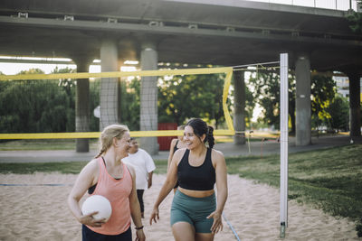 Smiling female friends walking while playing volleyball