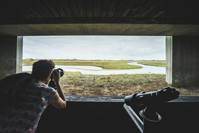 Rear view of man photographing through window