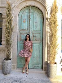 Full length portrait of young woman standing against door