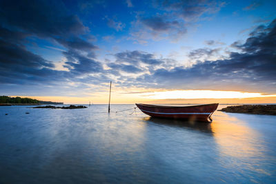 Boat moored in sea against sky during sunset
