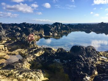 Naked man crouching on rock formation against sky