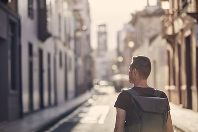 Rear view of man standing on street against buildings in city