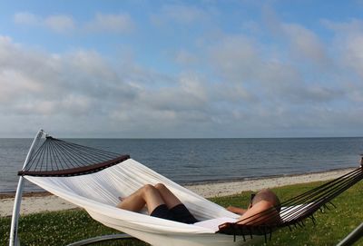 Man relaxing in hammock against sea and cloudy sky