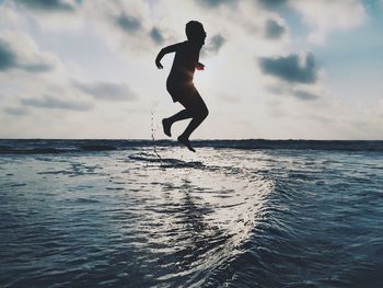 Silhouette woman jumping in sea against sky at sunset