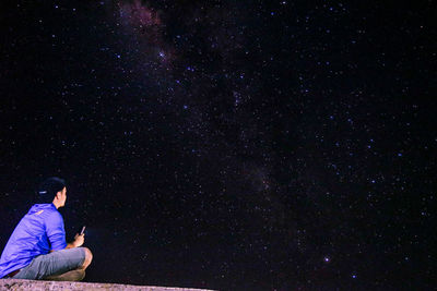 Side view of man sitting against star field at night