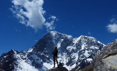 Man standing on snowcapped mountain against blue sky
