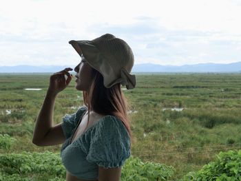 Side view of young woman looking away while standing on field against sky