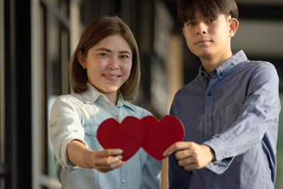 Portrait of smiling couple holding heart shape while standing outdoors