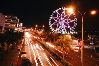 Light trails on illuminated city against sky at night