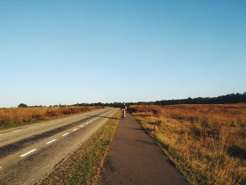 Road amidst field against clear sky