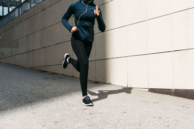 Low section of woman jogging on footpath by wall