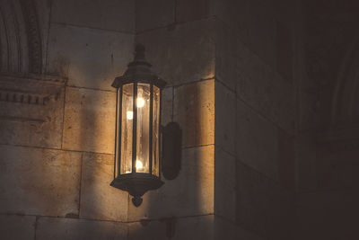 Low angle view of illuminated light bulb hanging against wall