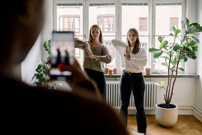 Teenage girl with mobile phone filming female friends dancing against in living room