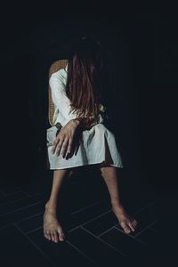 Full length of spooky woman sitting on chair in darkroom