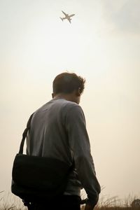 Rear view of man looking at airplane against sky