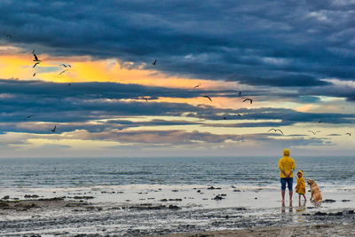 Rear view of men on beach against sky during sunset