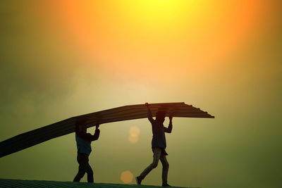 Silhouette people standing against orange sky