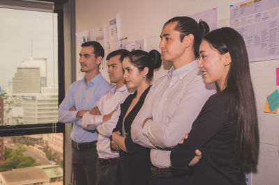 Smiling colleagues standing by wall in office