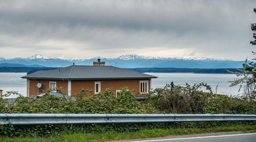 House by lake and buildings against sky