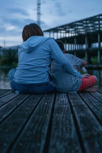 Rear view of woman sitting on pier against sky