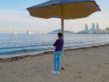 Rear view of man standing at beach against sky