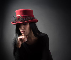 Portrait of beautiful young woman wearing hat against black background