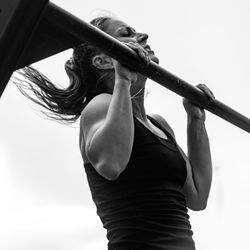 Low angle view of athlete practicing chin-ups against sky