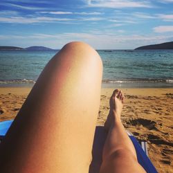 Low section of person relaxing on beach against sky