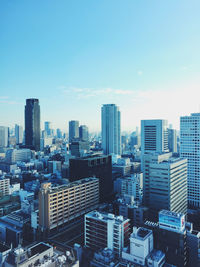 The sun shines through a blue sky on to tall buildings from high above in osaka, japan.