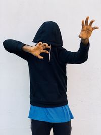 Young man wearing hood gesturing while standing against white background