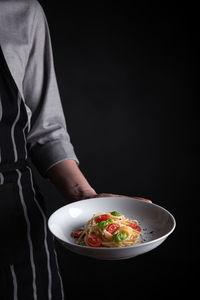 Midsection of person holding bowl against black background