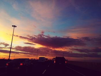 Cars on road against sky at sunset