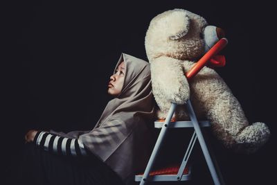 Girl with teddy bear against black background