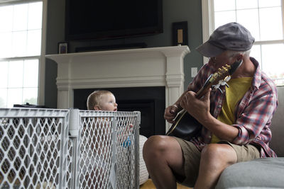 Grandson looking at grandfather playing string instrument at home