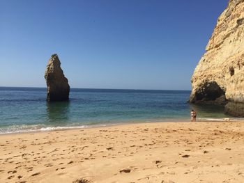 Scenic view of rocks on beach against clear blue sky