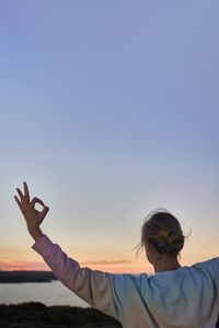 Side view of man with arms raised against clear sky