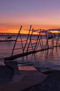 Silhouette wooden posts on beach against sky during sunset