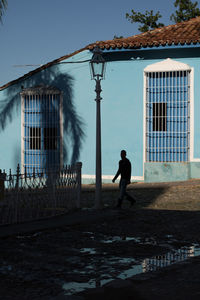 Silhouette man standing outside house against sky