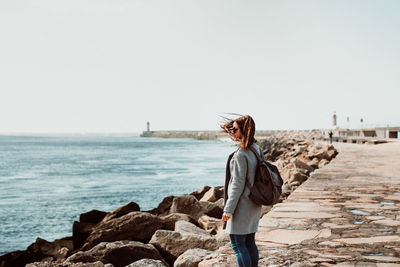 Side view of woman wearing backpack while standing on pier over sea against clear sky